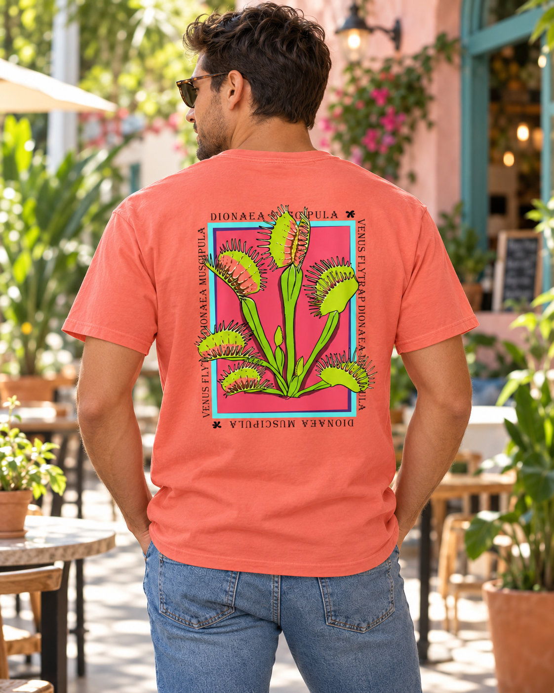 Man wearing the Bright Salmon unisex Venus Flytrap graphic tee, showing the back artwork in a café courtyard.