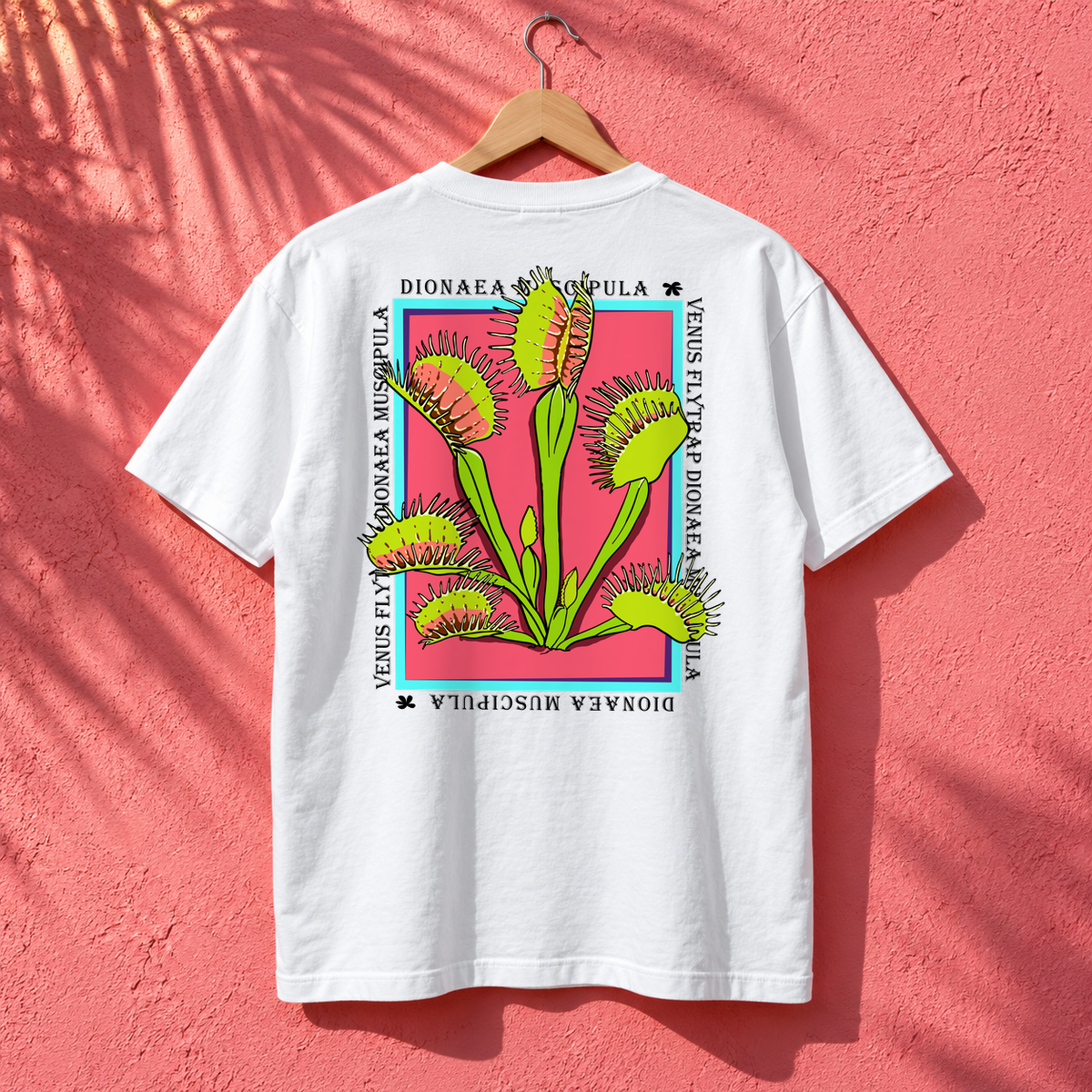 White Venus Flytrap graphic tee hanging against a pink wall, showing the large botanical back print.