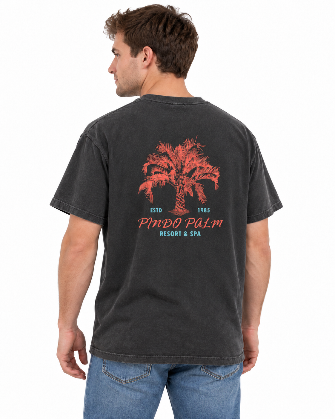 Rear-left studio view of a man wearing the Pepper Pindo Palm t-shirt with the original coral and turquoise back graphic.