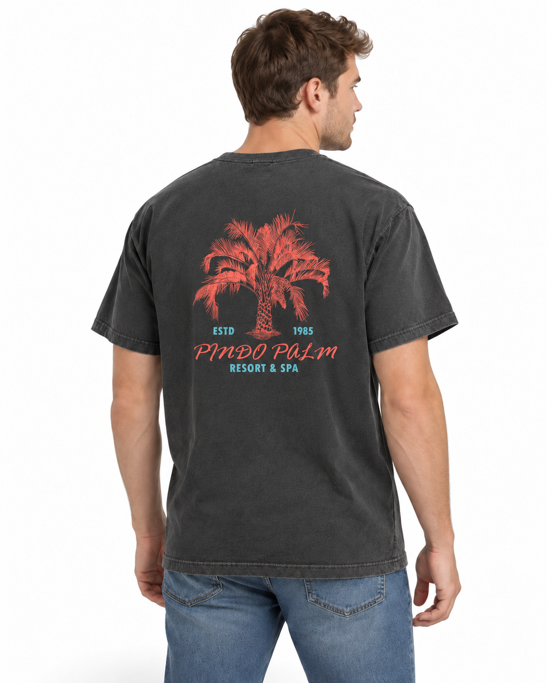 Rear-right studio view of a man wearing the Pepper Pindo Palm t-shirt with the original coral and turquoise back graphic.
