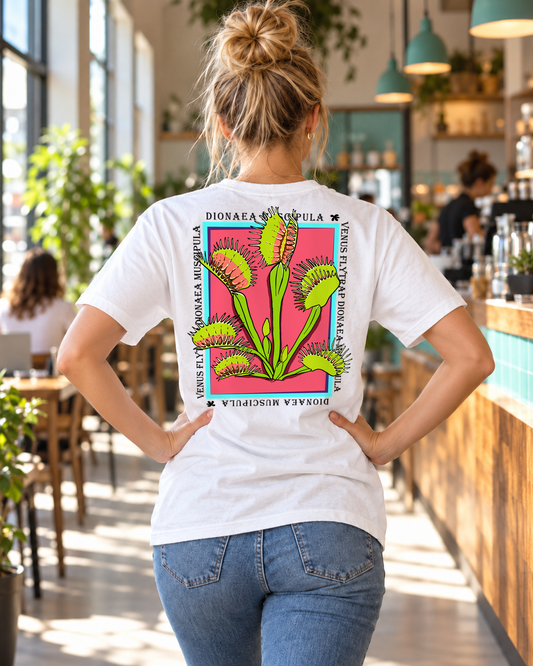 Woman wearing the white Venus Flytrap graphic tee, showing its colorful back print in a cafe.